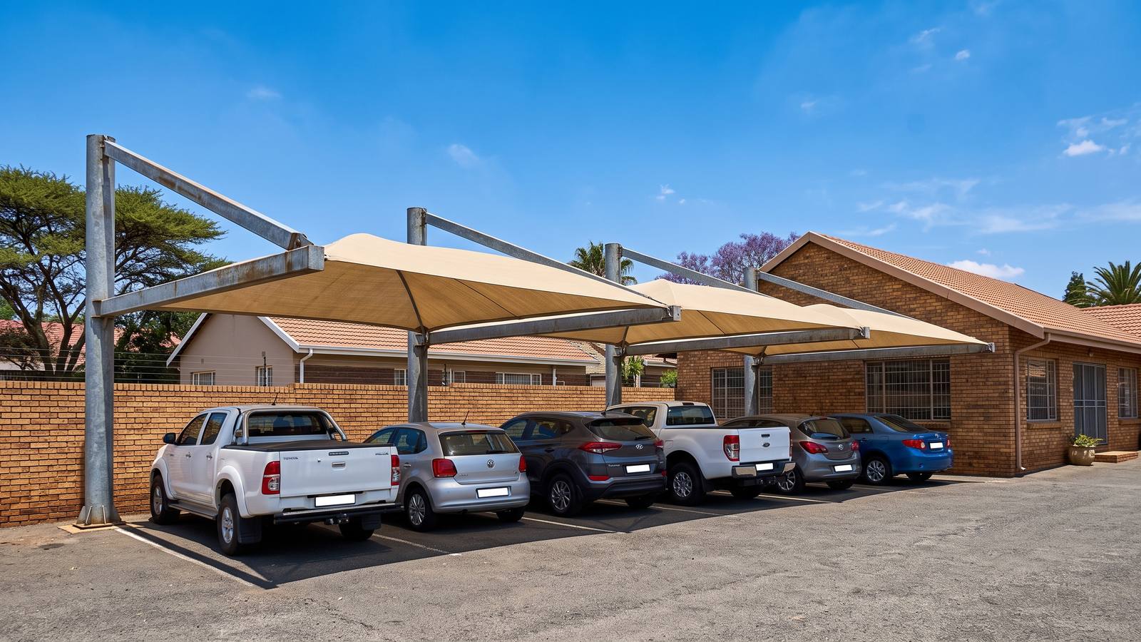 Cantilever shadeport with beige shade net over six parking bays, columns along the back only.